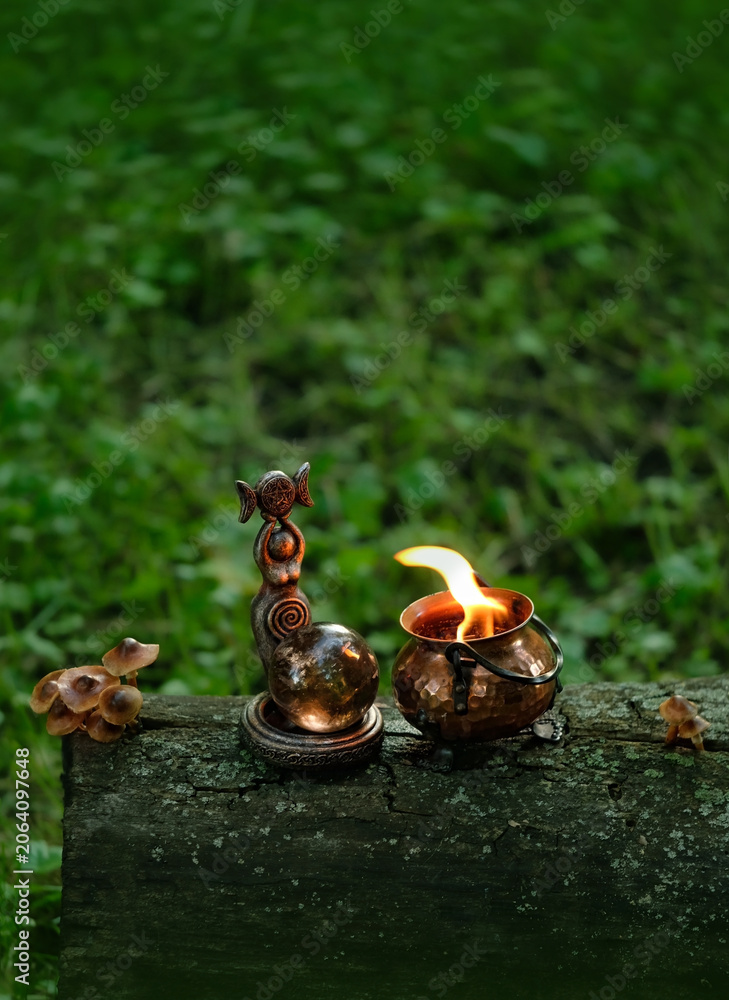 Obraz premium wiccan Goddess figurine with crystal ball and burning witch cauldron in forest, dark natural background. esoteric spiritual practice. magic ritual, witchcraft. mystery, fairy tale atmosphere
