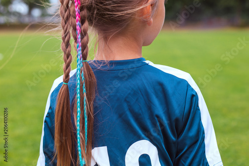 Obraz na plátne Young girl with braided hair wearing a blue football jersey stands on a grassy f