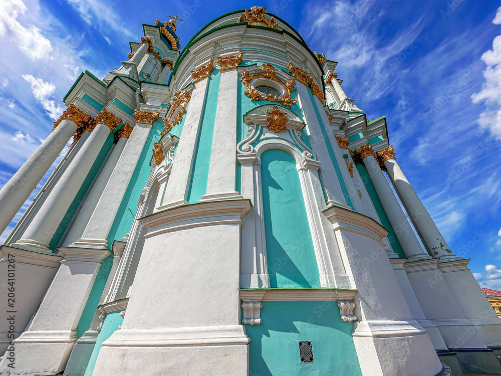 Naklejka premium Low angle view of a beautiful baroque church with turquoise walls and gold decorations under a bright blue sky.