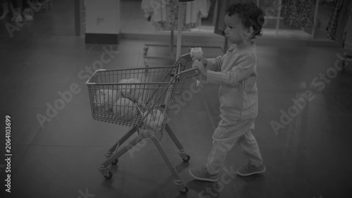 Toddler Pushing Small Metal Shopping Cart Filled with Clothes in Boutique