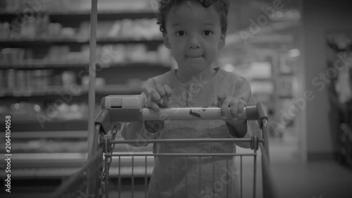 Toddler seated in supermarket shopping cart gripping handle