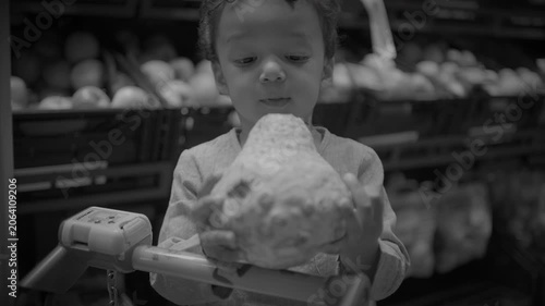Child sitting in shopping cart holding a cauliflower in supermarket produce aisle