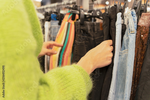 Close up of a person's hand browsing through a rack of casual clothing in a shop, concept of fashion retail, personal style discovery, and smart shopping.