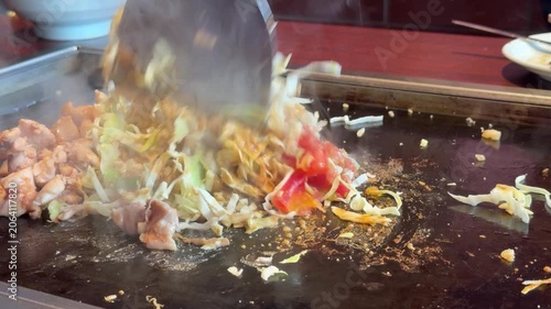 日本のもんじゃ焼き。鉄板焼き料理。カレー味のキャベツや鶏肉をコテで混ぜる動画。
