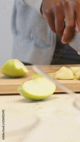 Vertical video: Entering right hand, slicing half green apple for snack on wood board, knife