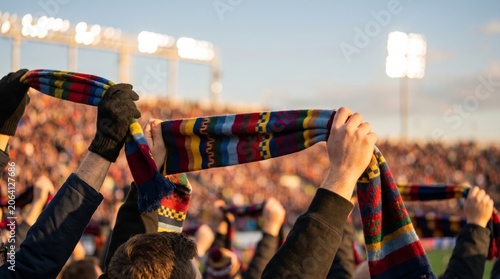 Excited fans raising colorful scarves in unison during a vibrant match at sunset.