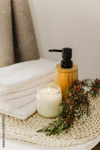 Minimalist still life of luxury spa essentials. White cotton towels with visible textured, bottle with oil and soy wax candle.