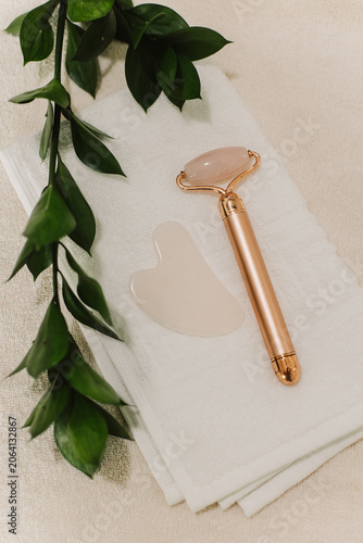 Facial rose quartz stone massage roller and gua sha massager on a white towel background.