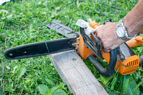 Schilderij op canvas Man hand holding electric chainsaw on wooden plank