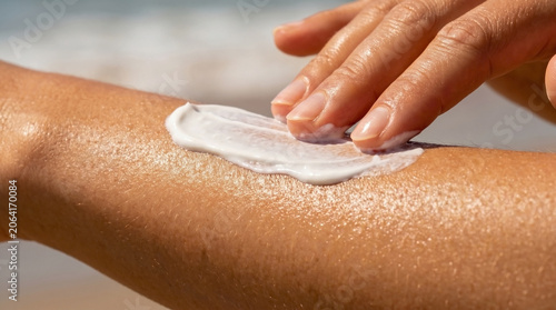 Hand applying sunscreen onto sun-kissed skin, extreme close-up of creamy texture showing hydration. Detailed shot emphasizes smooth protection, glowing healthy skin.