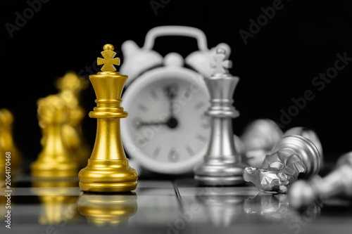 фотографія Golden chess king standing before defeated silver pieces and alarm clock on chessboard representing strategy