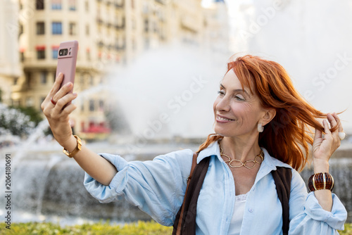 Quadro em tela Smiling mature woman taking a selfie with windblown hair in the city