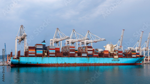 Tableau sur toile Cargo ship unloads containers at busy port in sunlight with cranes in background