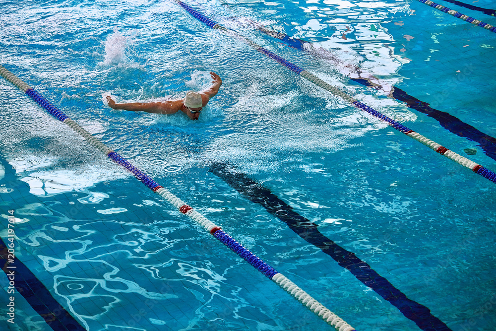 Naklejka premium Male swimmer practicing backstroke with water splash in pool. Concept of competitive swimming, sports training, aquatic fitness, and performance improvement.