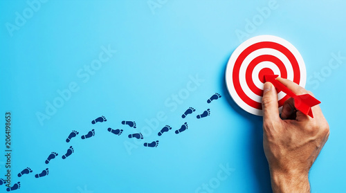 Business Goal Achievement and Target Success Concept with Hand Hitting Bullseye and Strategic Path to Growth on Blue Background
