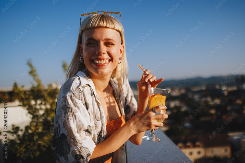 Obraz premium Happy woman toasting a cocktail on urban rooftop at sunset