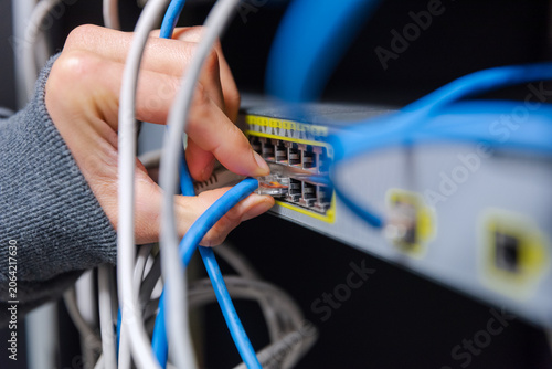 Canvas Print Close-up of a technician's hands organizing and plugging blue and grey ethernet network cables into a network switch