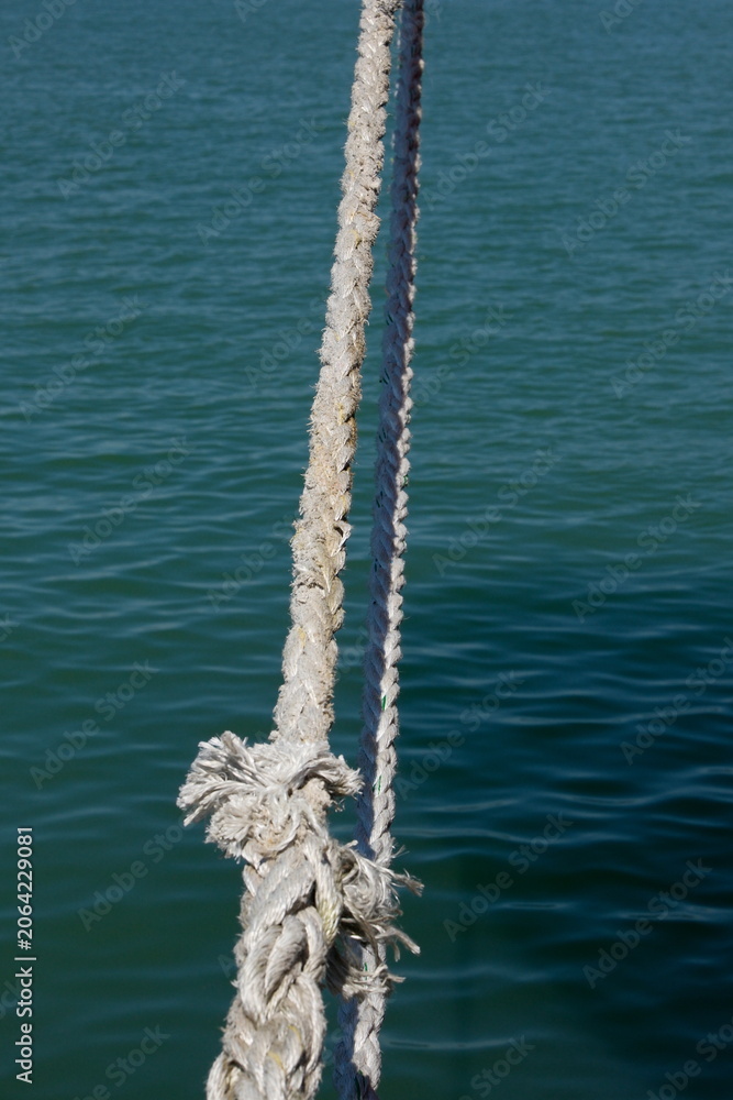 Fototapeta premium Close-up of a sunlit nautical rope with blurred blue sea water surface on background, summer travel concept.