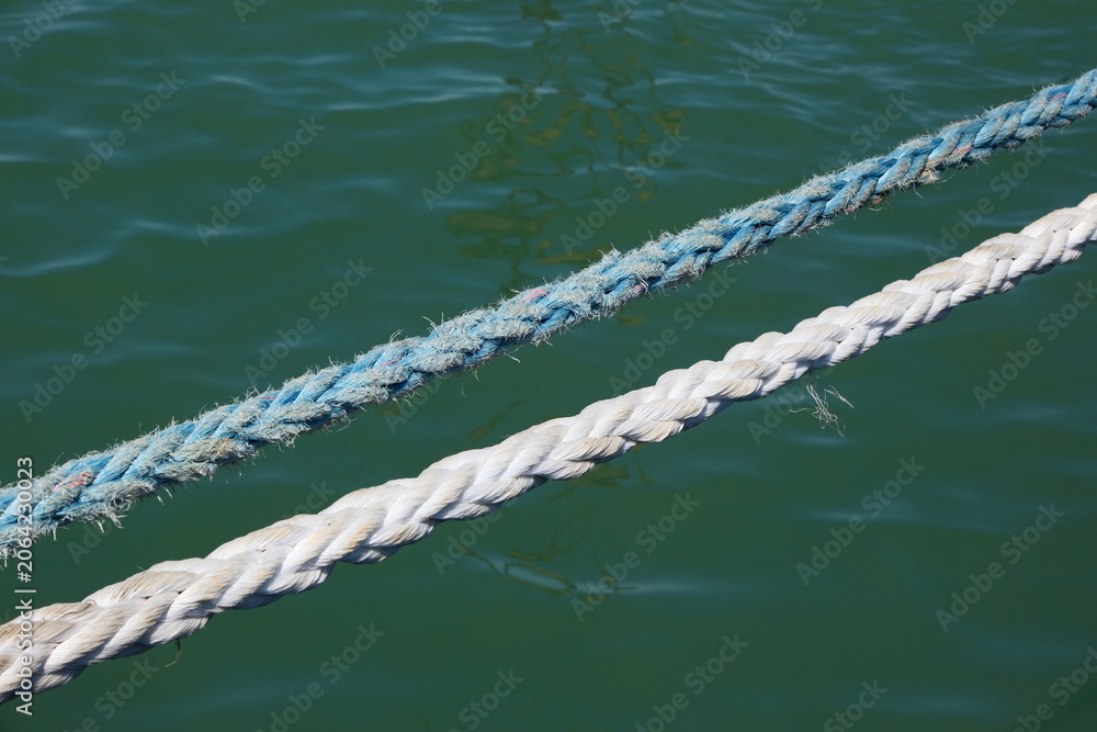 Fototapeta premium Close-up of a sunlit nautical rope with blurred blue sea water surface on background, summer travel concept.