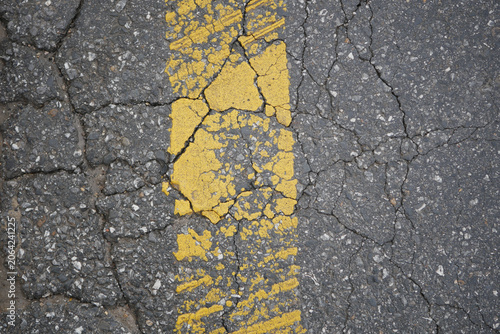 Fotografi Cracked road with faded yellow line in urban area