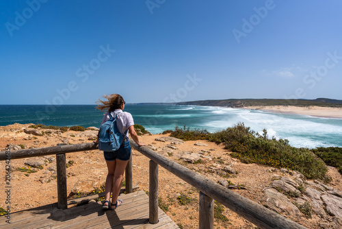 Visiting Algarve coast in Portugal. Beautiful middle-aged woman tourist standing  at Carrapateira viewpoint and enjoying vacations over ocean on summer day. Back view