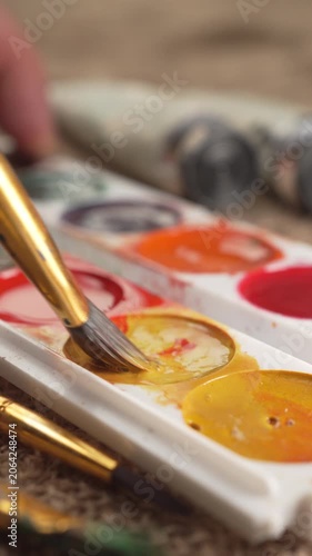 A close-up of a watercolor palette, with a brush picking up orange. Hobbies and leisure concept
