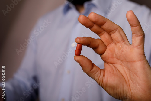 Close-up of a hand holding a red capsule medication for health.
