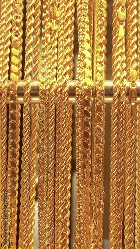 Close-up of multiple gold necklaces and chains hanging on a display rod with subtle shimmering movement in a jewelry shop