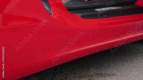 Horizontal day city street video close up. White woman places female legs in stiletto high heel shoes on asphalt and gets out of red sport car. Concept of beauty, fashion, glamour, walk, luxury, gloss