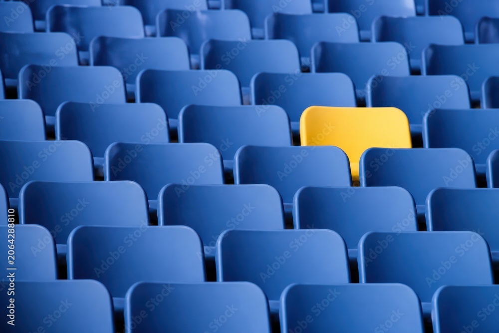 Fototapeta premium Empty stadium seats with one yellow seat among blue rows