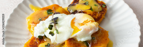 Millet pancakes are served on a plate with hollandaise sauce and a poached egg. This meal is ideal for anyone looking for a healthy breakfast or lunch option, banner