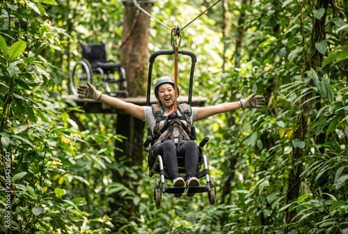 Exhilarated young woman using an adaptive zip-line seat with outspread arms in a lush tropical rainforest