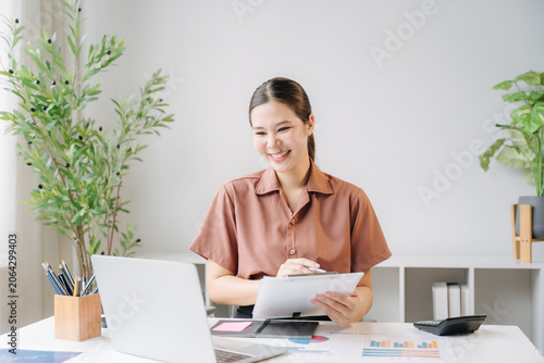 Φωτογραφία Productive Workday: A smiling woman is working at her desk with a laptop, clipboard, and calculator