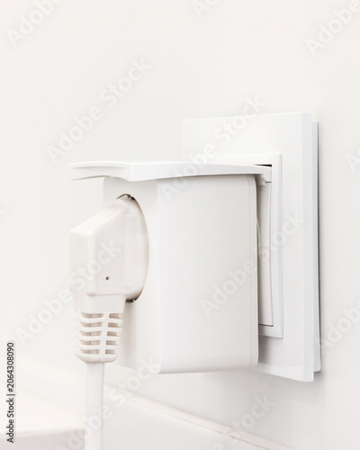 White electrical plug connected to wall socket on bright, clean background. Modern power connection with simple, minimalist design