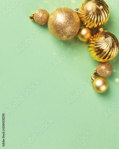 Gold Christmas ornaments on light green background. Holiday decoration features glittery, swirl, and smooth baubles, top view with ample copy space for text