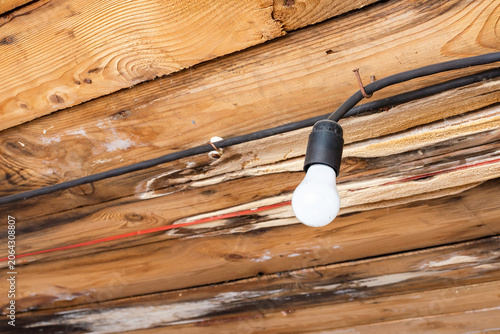 Bare old light bulb hanging from a rustic unfinished wooden ceiling. Industrial rustic style lighting in an old abandoned wooden building renovation. copy space.