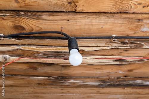 Bare old light bulb hanging from a rustic unfinished wooden ceiling. Industrial rustic style lighting in an old abandoned wooden building renovation. copy space.