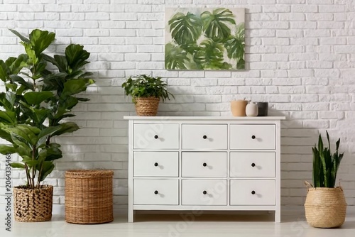 Green houseplant on commode and painting hanging at white brick wall in living room
