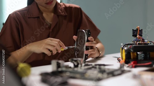 Young female technician using a screwdriver to disassemble and repair a computer hard drive while working on a robotics project in a science and technology laboratory for data recovery