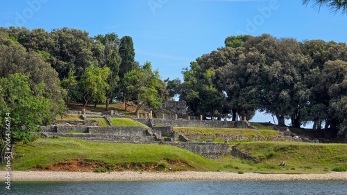 Ancient Stone Ruins Amidst Green Trees and Blue Sky by Water