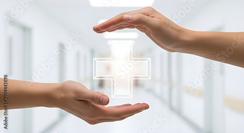 Medical professional hands holding glowing cross symbol as concept of health care safety.