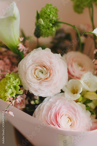Close-up of a delicate wedding bouquet featuring pale pink ranunculus flowers and white freesia. Soft focus, pastel floral background.