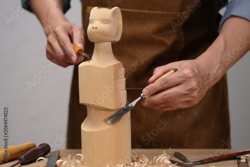 Artisan carving wooden sculpture with chisels on workbench with wood shavings