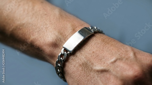 Close-up of a man's wrist wearing a shiny silver ID bracelet with a curb chain.