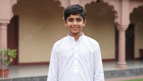 Portrait of a young boy smiling in a traditional white kurta in front of a building
