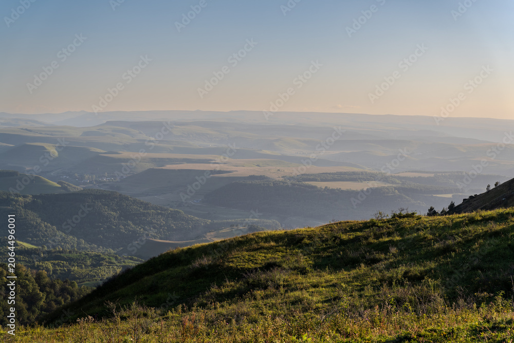 Fototapeta premium Layers of green mountains and hills in the haze during sunset. Panoramic View of Green hills and Meadow.