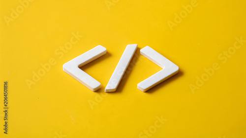 White plastic code brackets symbols for programming and web development isolated on a vibrant yellow background, representing software engineering