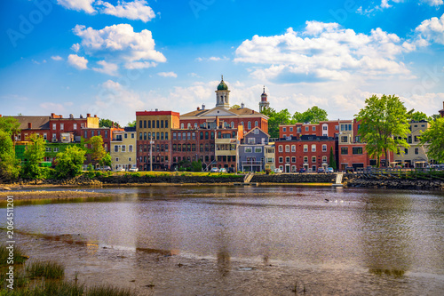 Historic brick buildings and church steeples in Exeter, New Hampshire, viewed across the Squamscott River on a clear summer day.