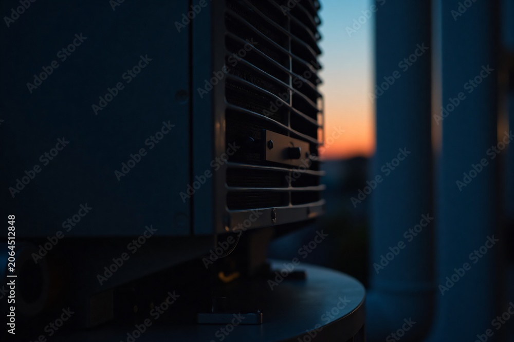 Naklejka premium Close-up view of industrial air conditioning unit with metal grilles during sunset showing mechanical and cooling system details in urban environment