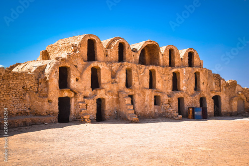 Scenic view of traditional three story clay ghorfas at Ksar Metameur fortified granary under a deep blue sky, Medenine, Tunisia.